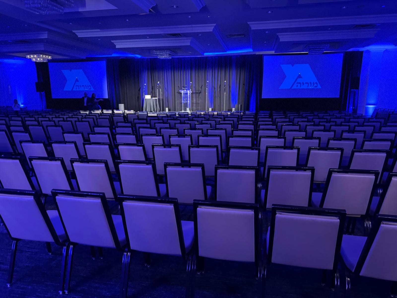 The ballroom set theater-style in blue light with two screens