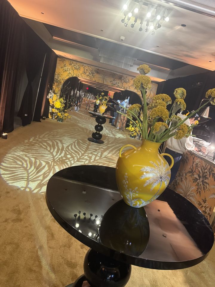 A yellow palm-painted vase of celosia on a black lacquer table, the palm-print arches beyond
