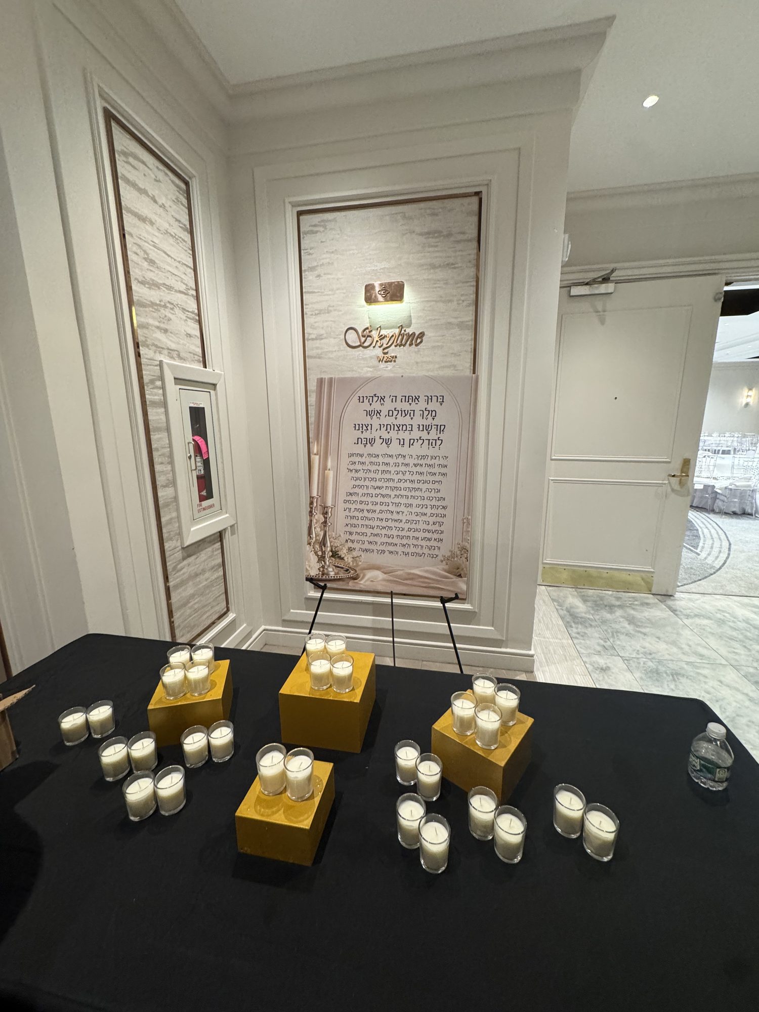 Shabbat candles set out for lighting at the door of Skyline West, the bracha on an easel beside them