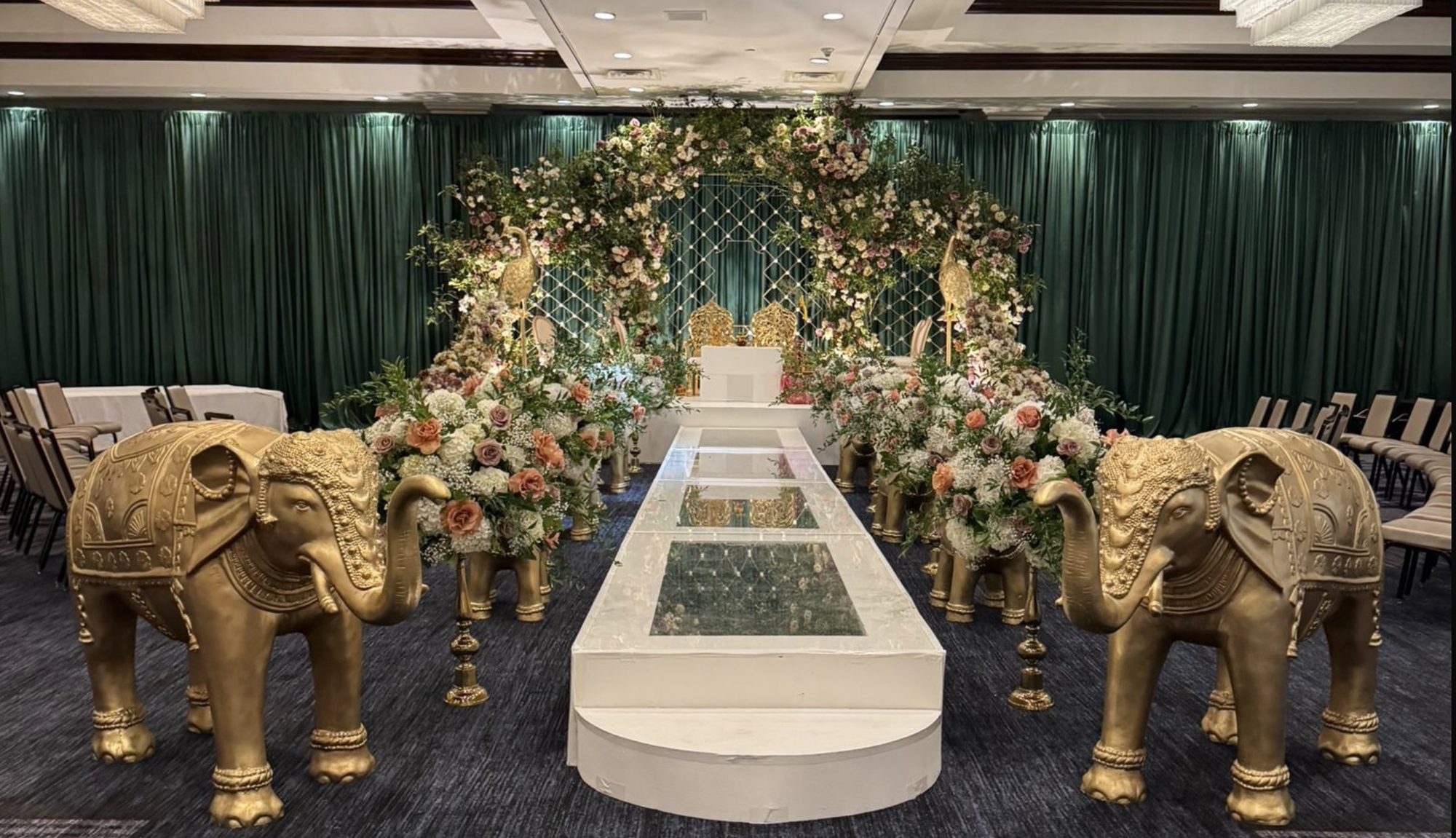 A mandap under a floral arch, gold elephants along the aisle