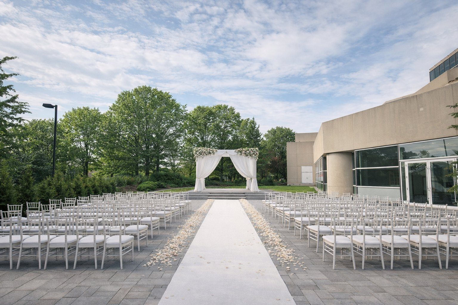 The patio set for a ceremony: white chairs, a white aisle and a floral arch